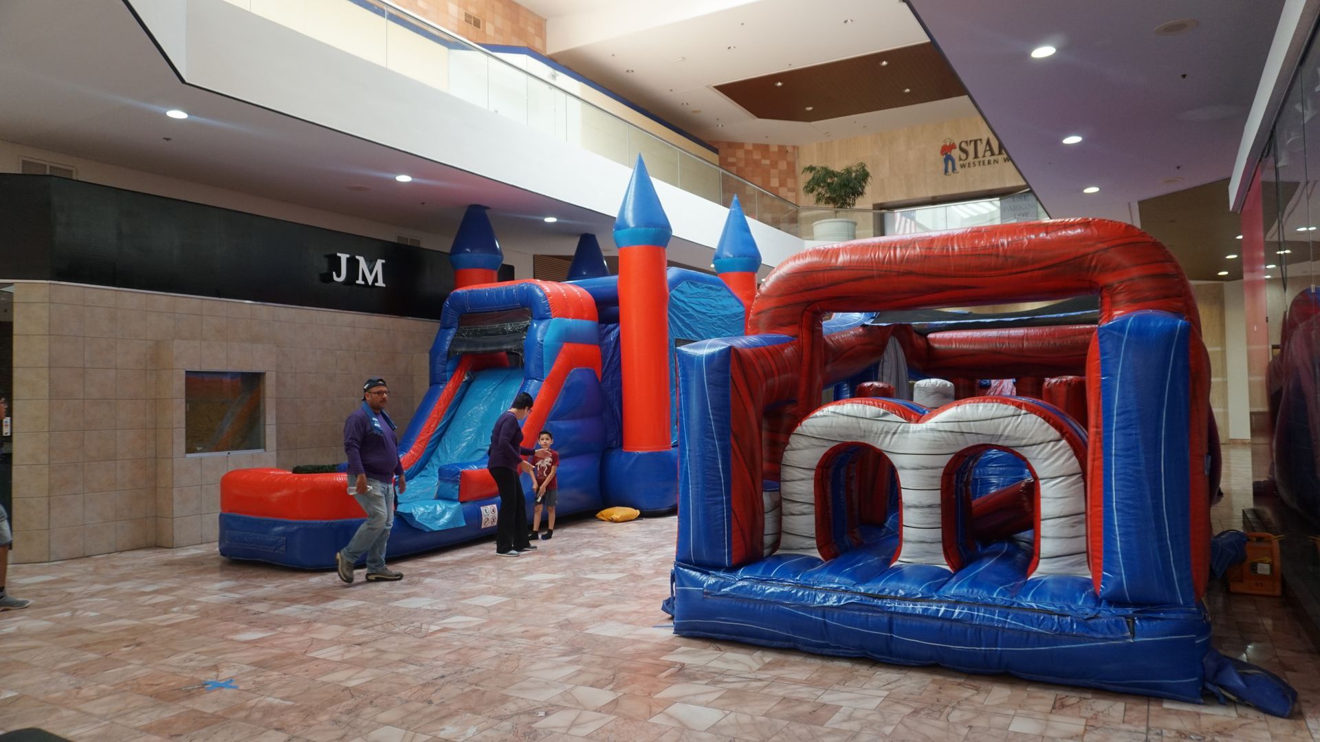Inflatable obstacle course and slides in a mall atrium, with a few children playing nearby.