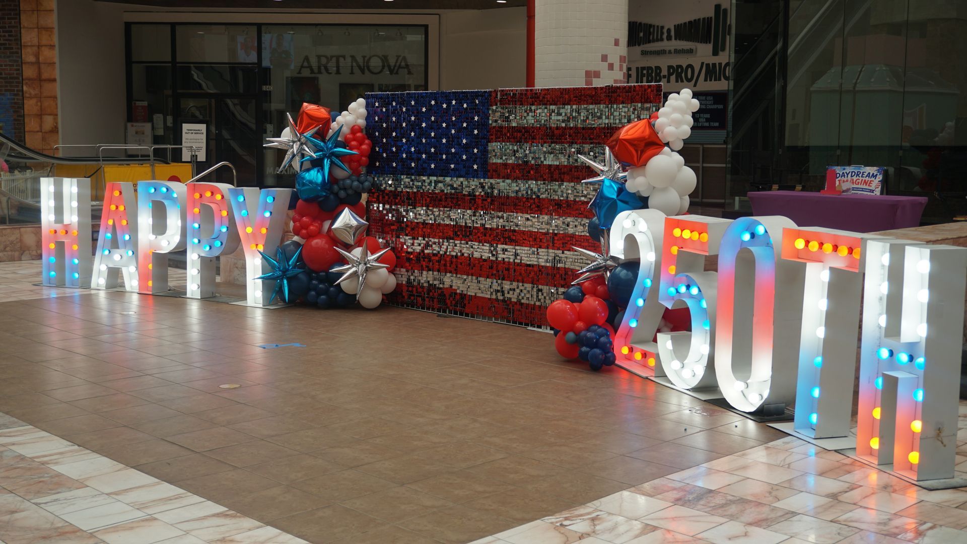 Festive mall display with illuminated “Indy 250th” letters, balloons, and an American flag backdrop