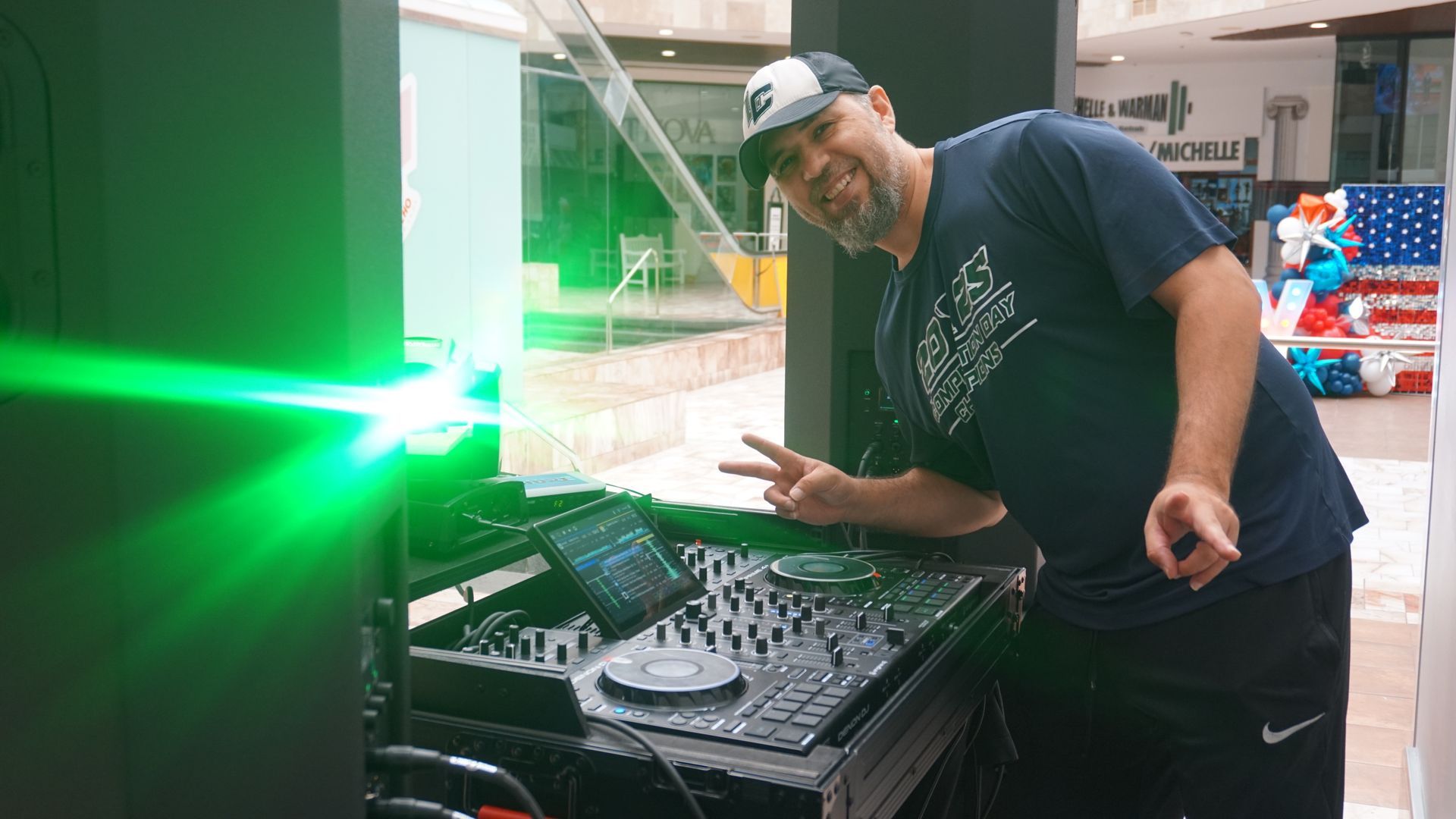 Man leaning over a DJ console beside a bright green laser light in a warehouse-like venue