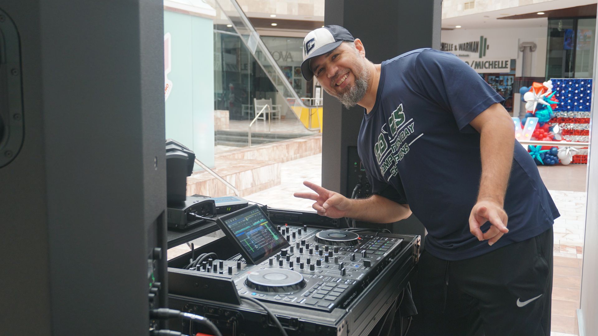 Man posing beside a DJ mixer in a shopping mall corridor