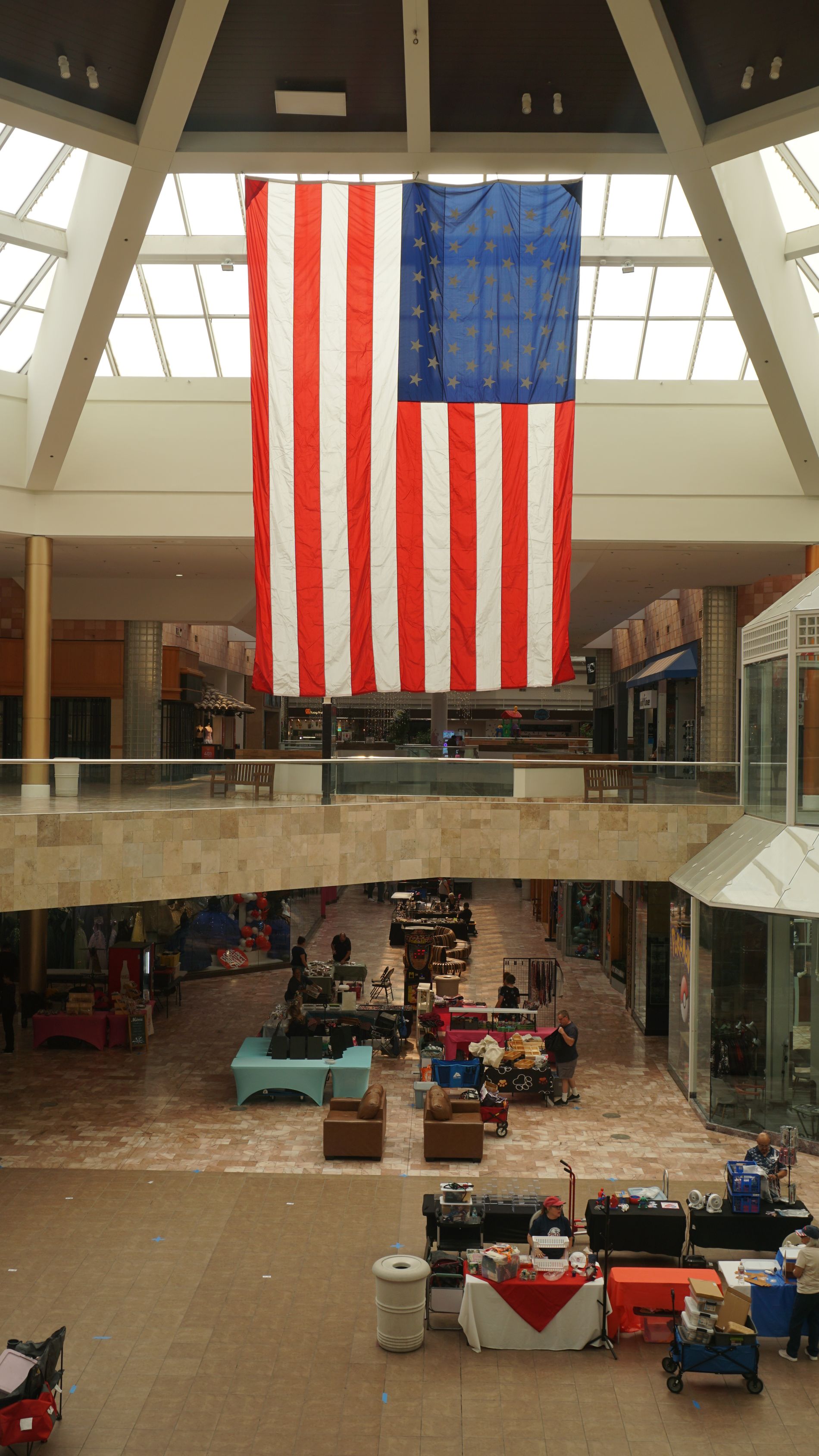 Large American flag hanging in a mall atrium above a crowded indoor market below