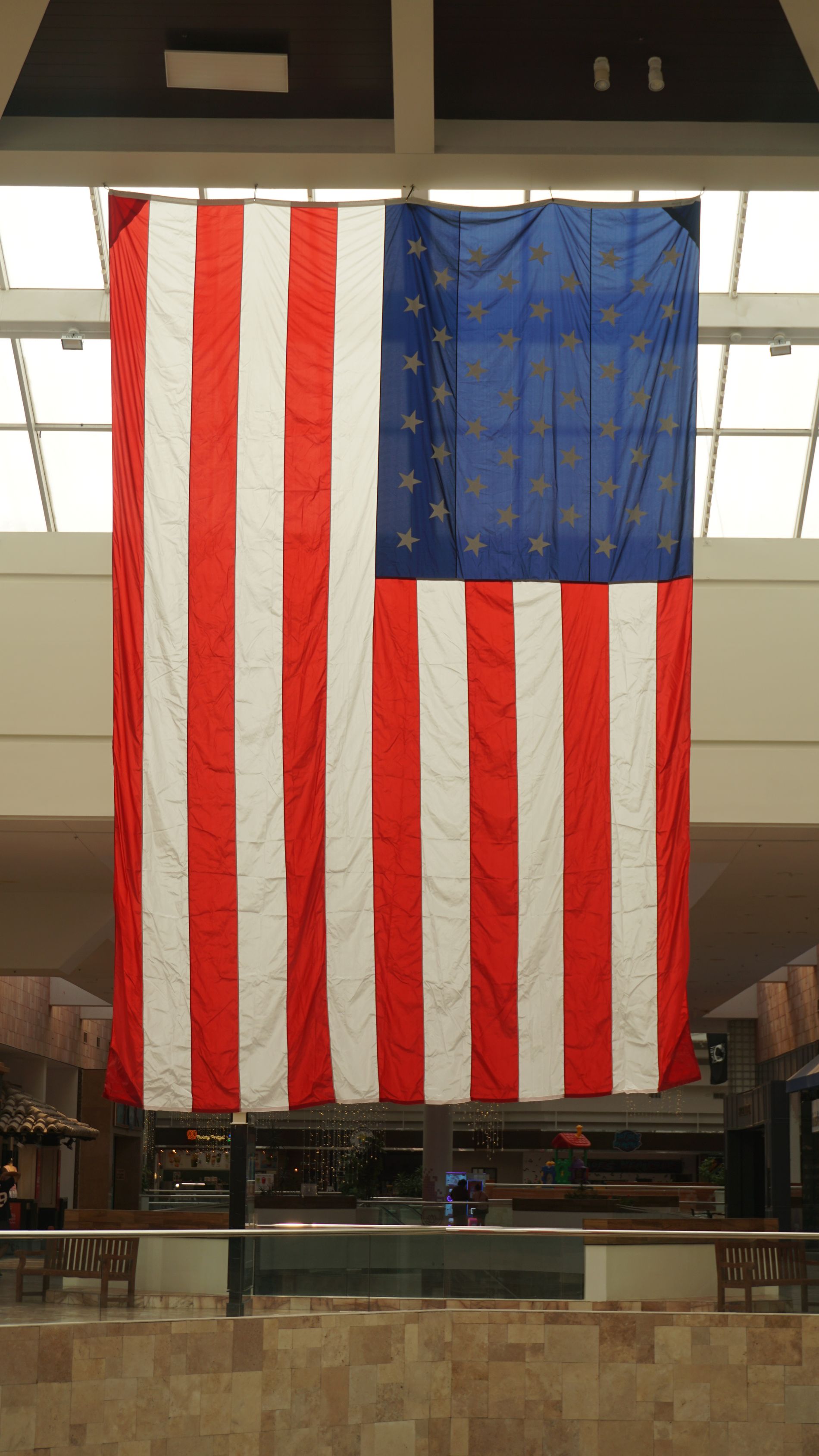 Large American flag hanging indoors from a high ceiling in a public building.