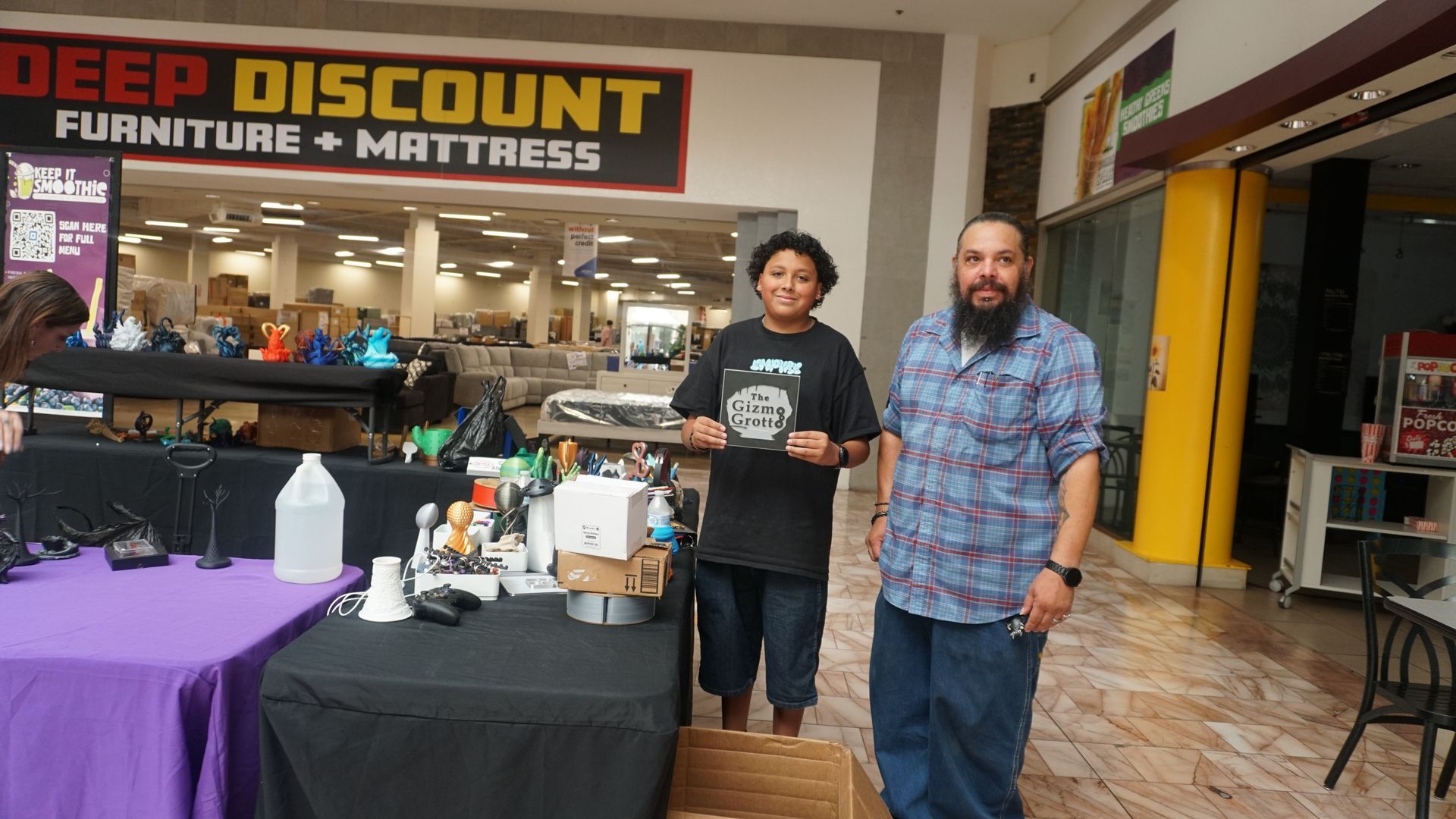Two men stand beside a table at a discount furniture and mattress store entrance