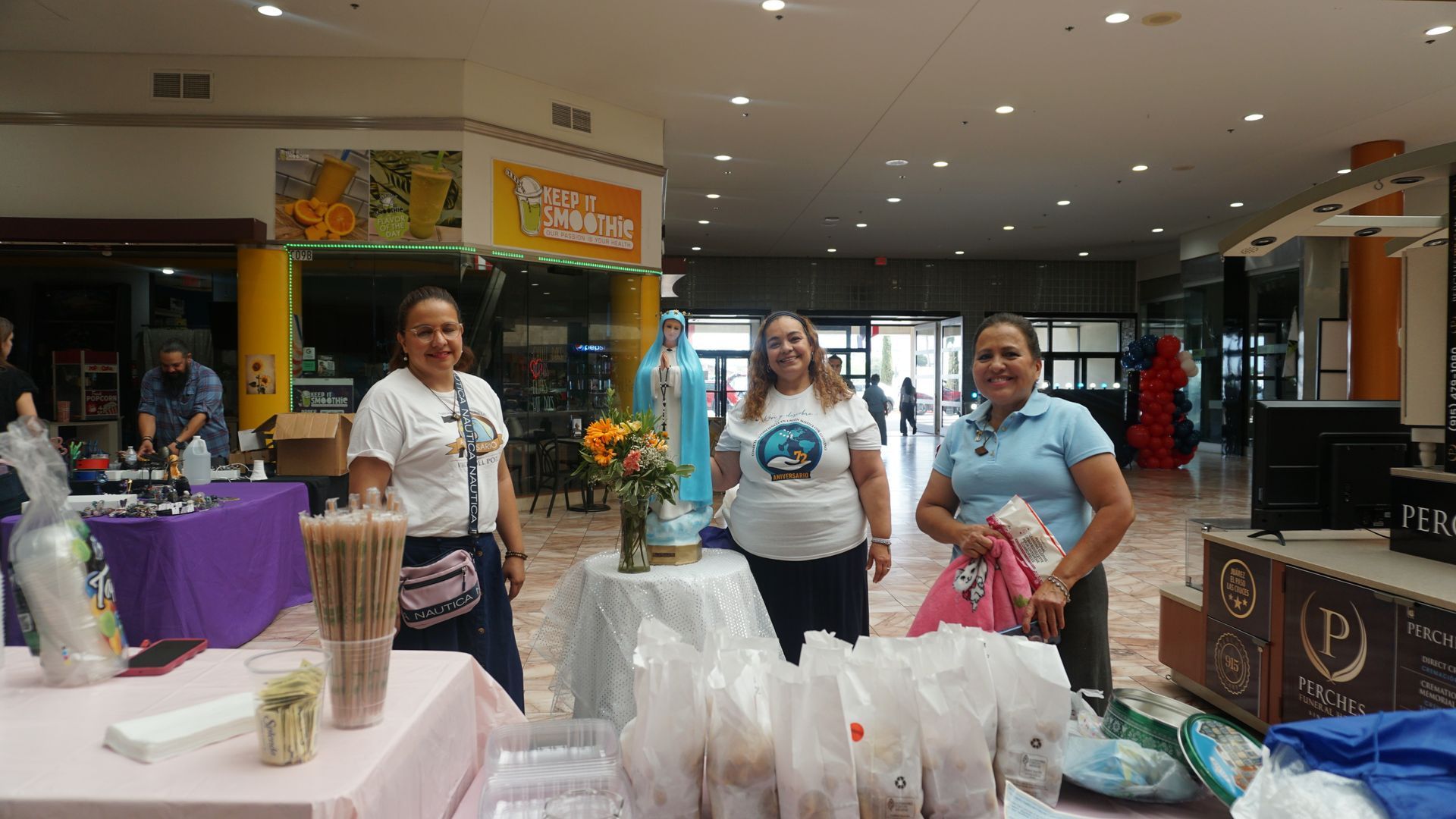 People standing at a mall booth with bags and products displayed on a table