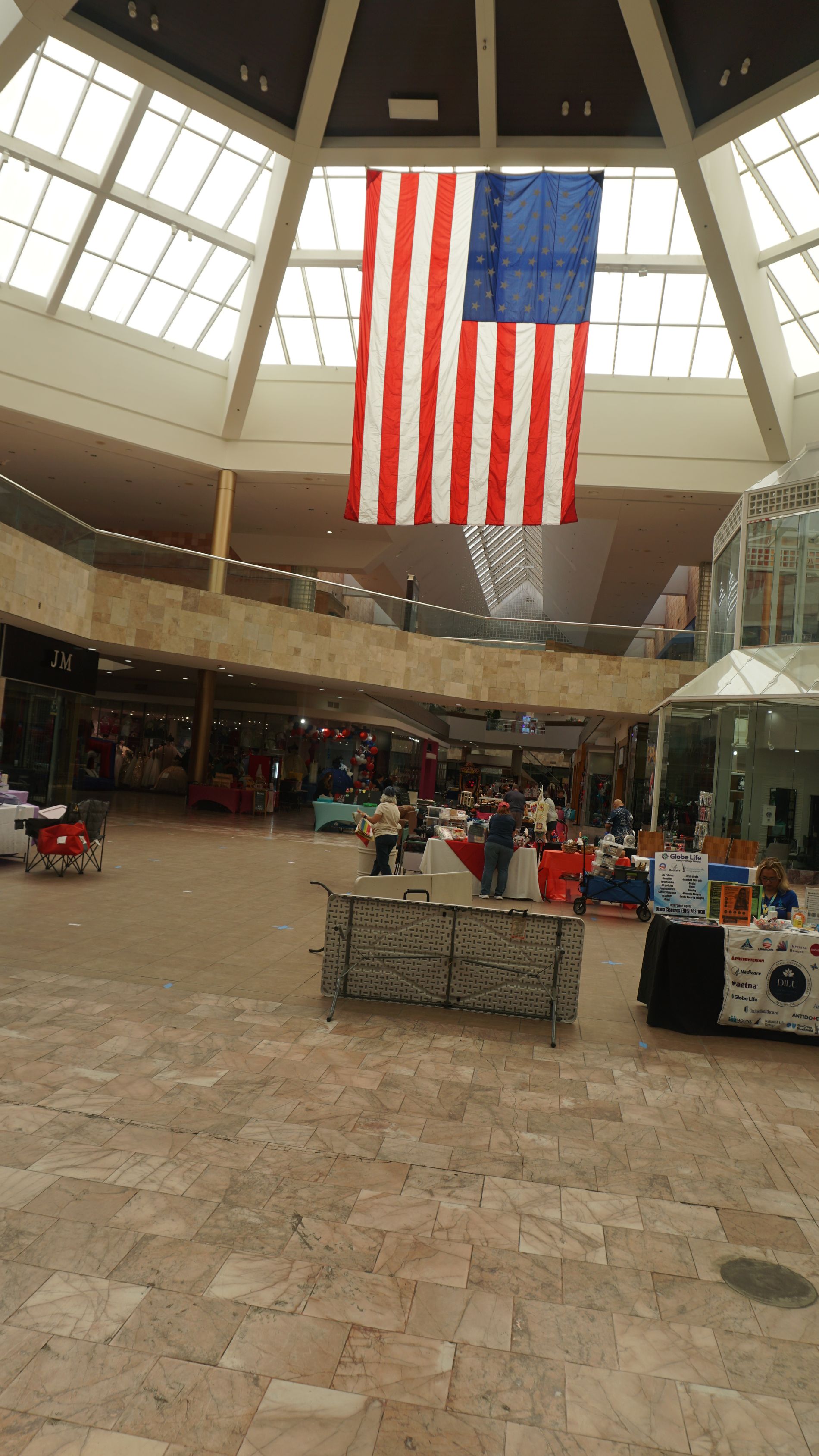 Mall atrium with a large hanging American flag under a domed skylight.