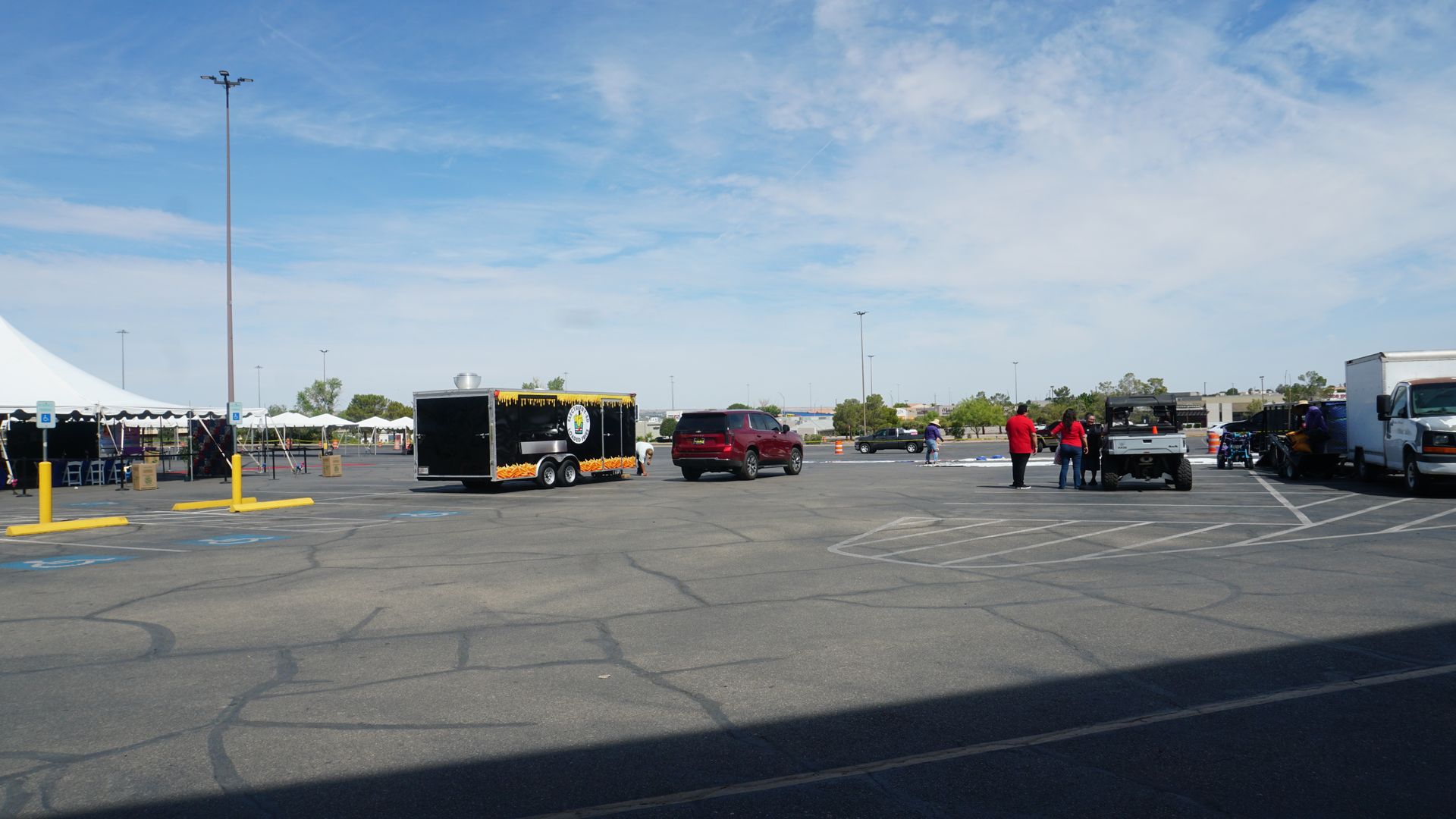 Parking lot with trailers and trucks under a blue sky, with a few people standing near vehicles.