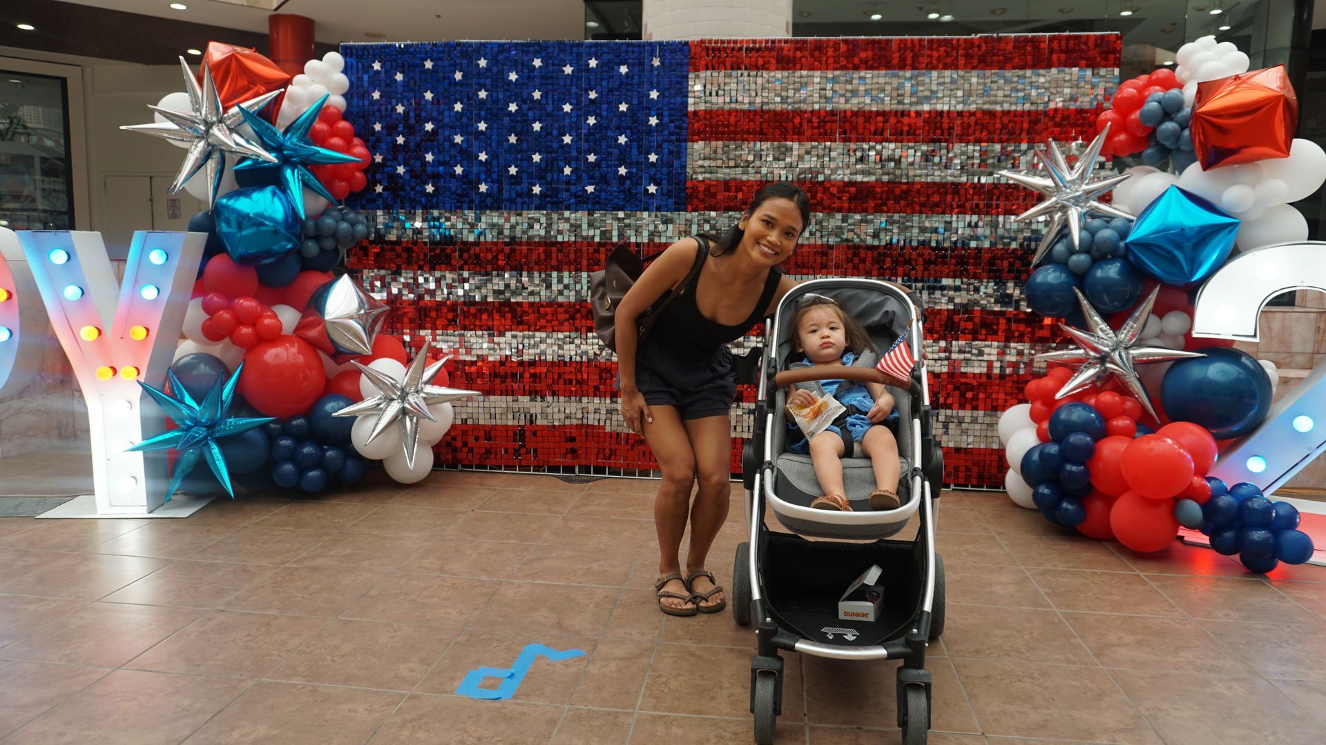 Woman leaning over a stroller in front of a large American flag backdrop with red, white, and blue decorations