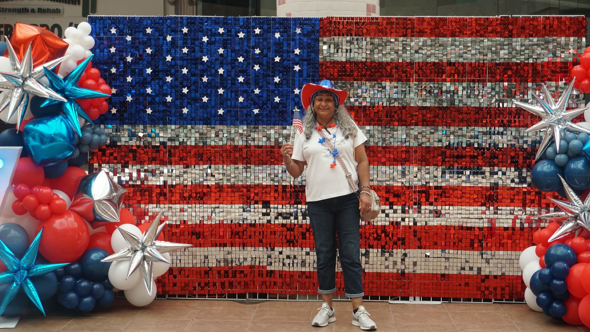 Person standing in front of a U.S. flag backdrop with red, white, and blue balloon decorations