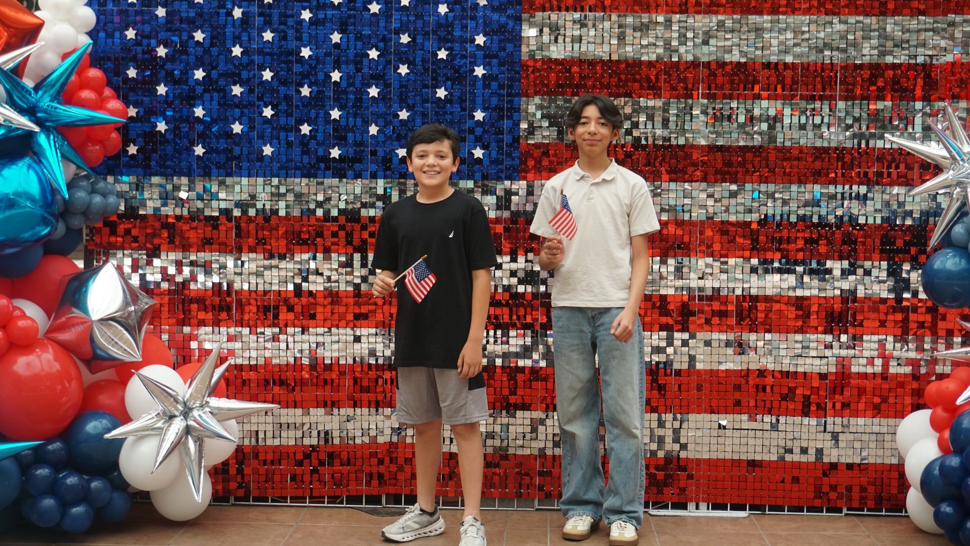 Two people posing in front of a red, white, and blue balloon American flag backdrop
