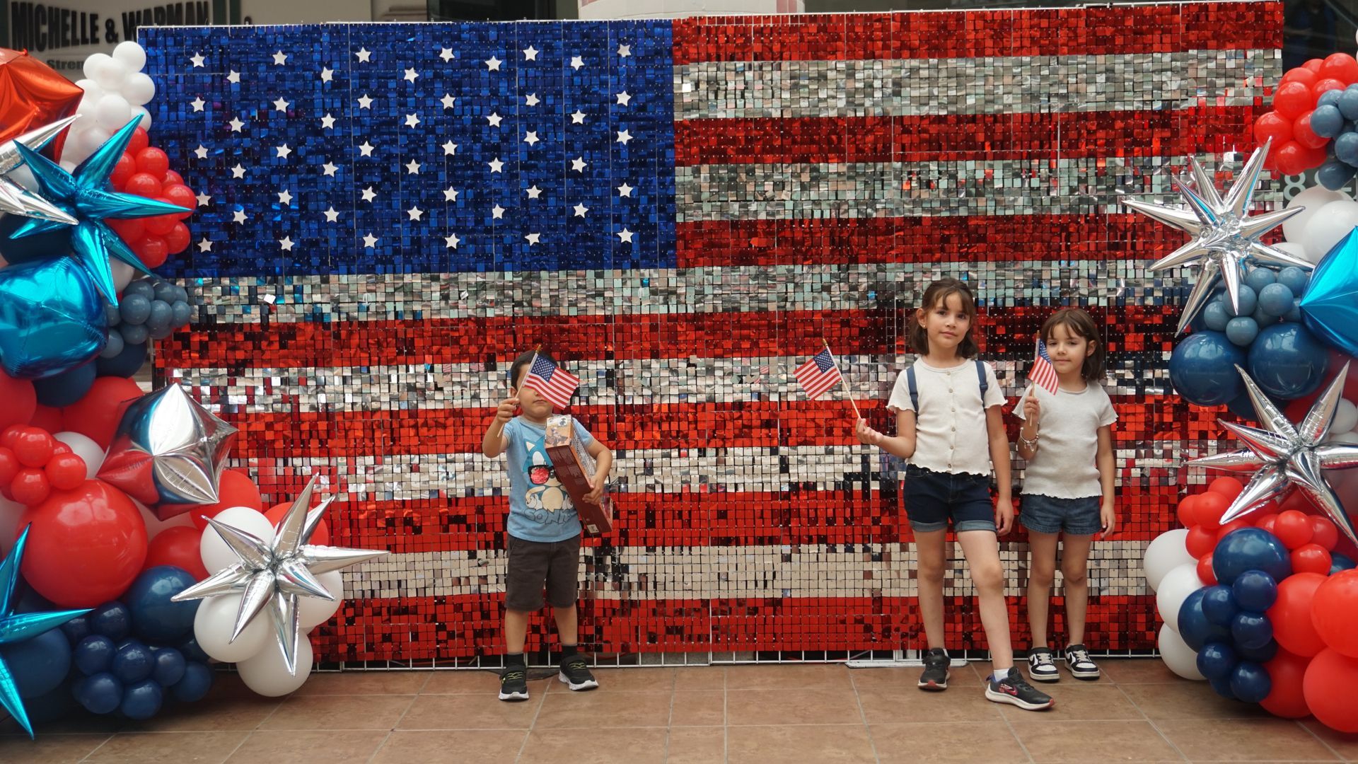 Kids posing in front of a large American flag made of red, white, and blue balloons