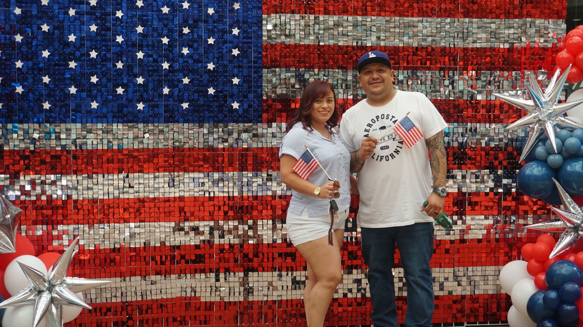 Couple posing before an American flag backdrop with red, white, and blue balloons
