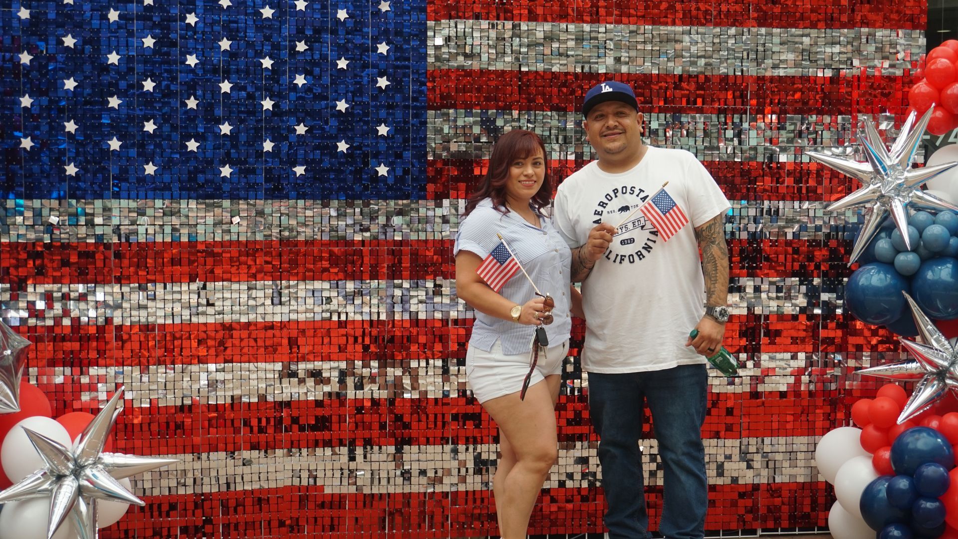 Couple posing before an American flag backdrop with red, white, and blue balloons and silver stars