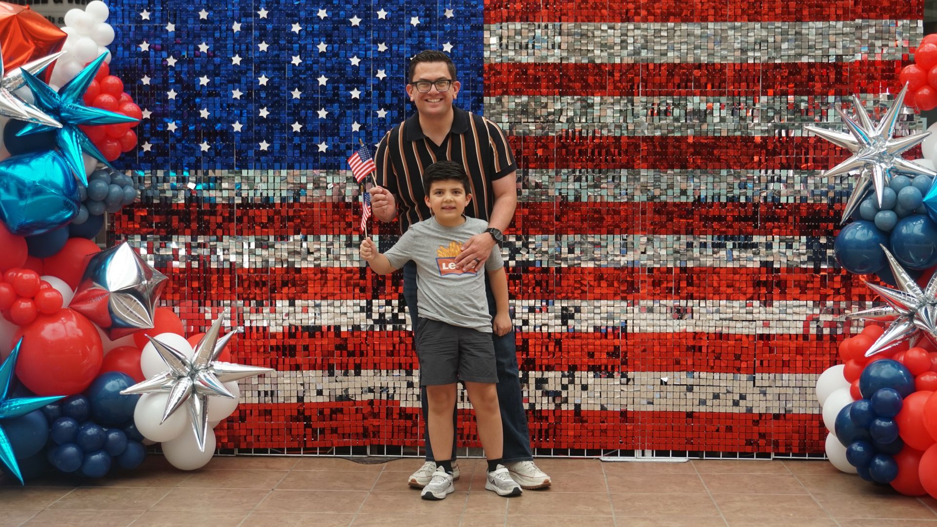 Man and child posing before a red, white, and blue American flag balloon backdrop