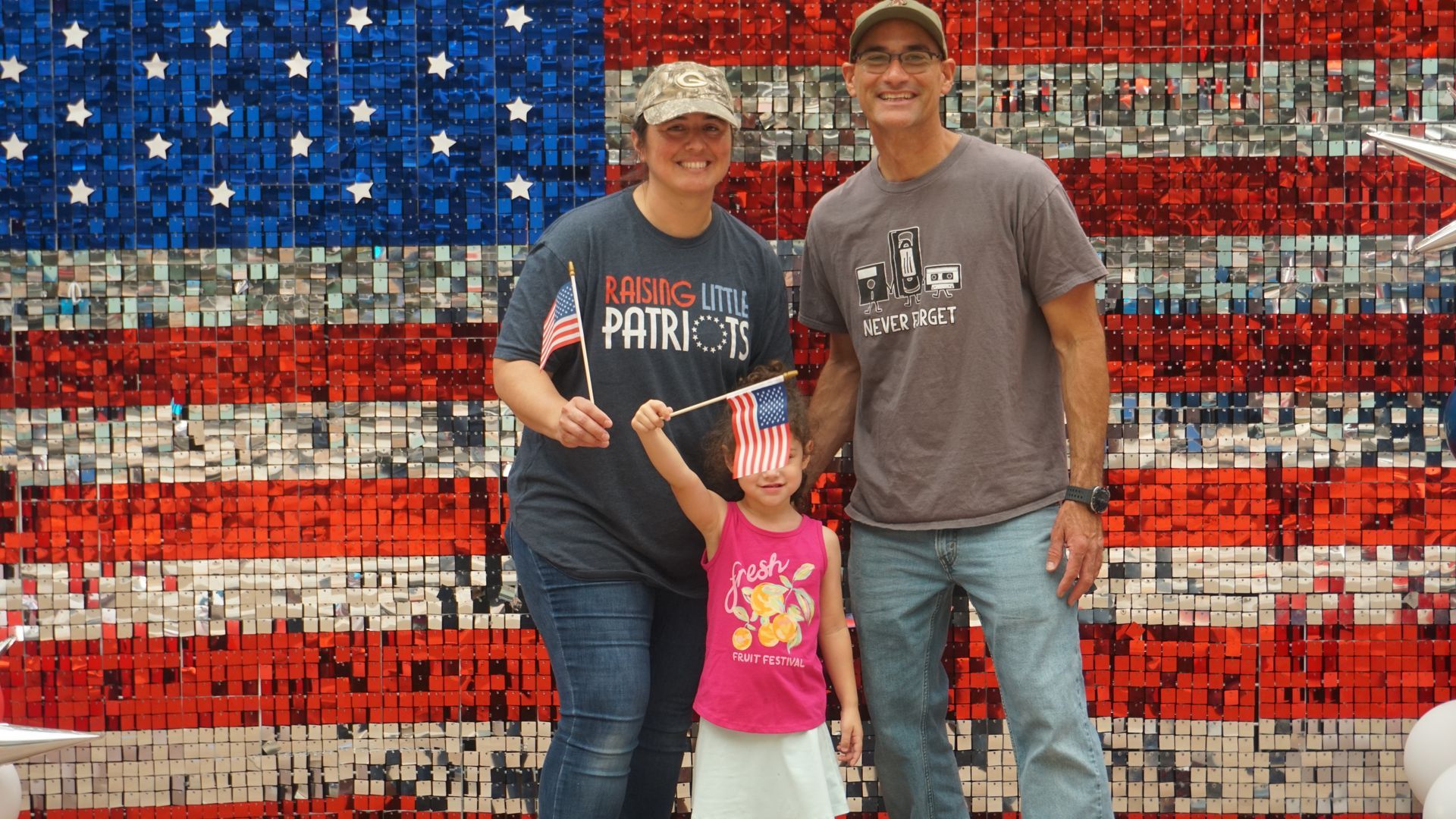 Three people posing in front of a red, white, and blue American flag mosaic wall.