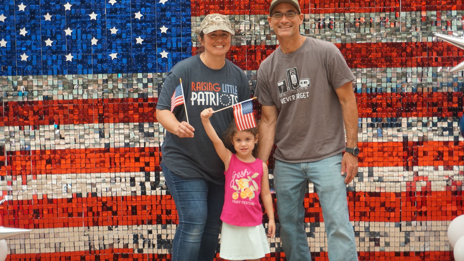 Three people posing in front of a red, white, and blue mosaic American flag mural