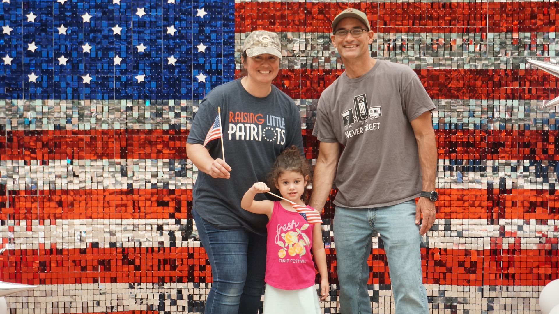 Family posing in front of a U.S. flag mural, with a child standing between two adults