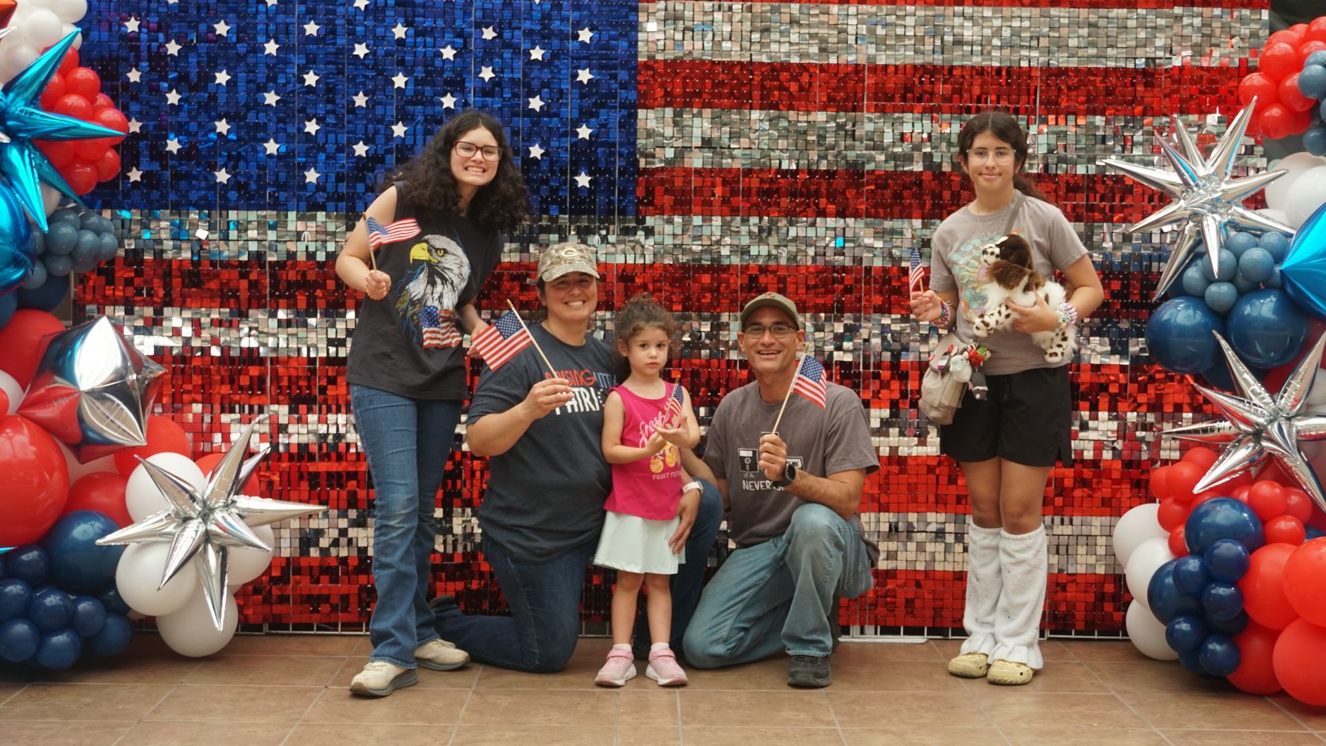 Five people posing before a red, white, and blue balloon American flag backdrop at a festive event