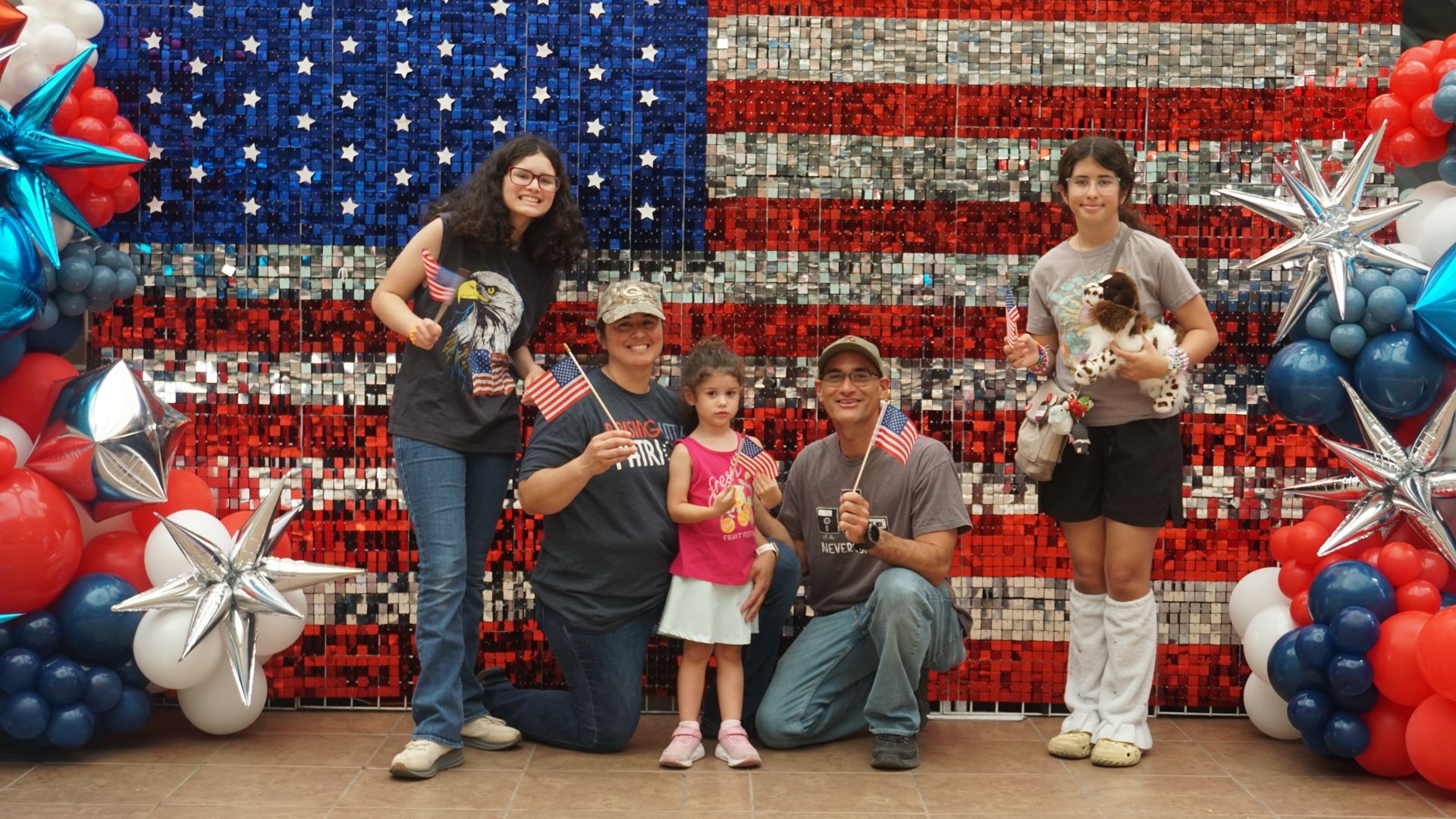 Group posing in front of a red, white, and blue patriotic backdrop with star balloons