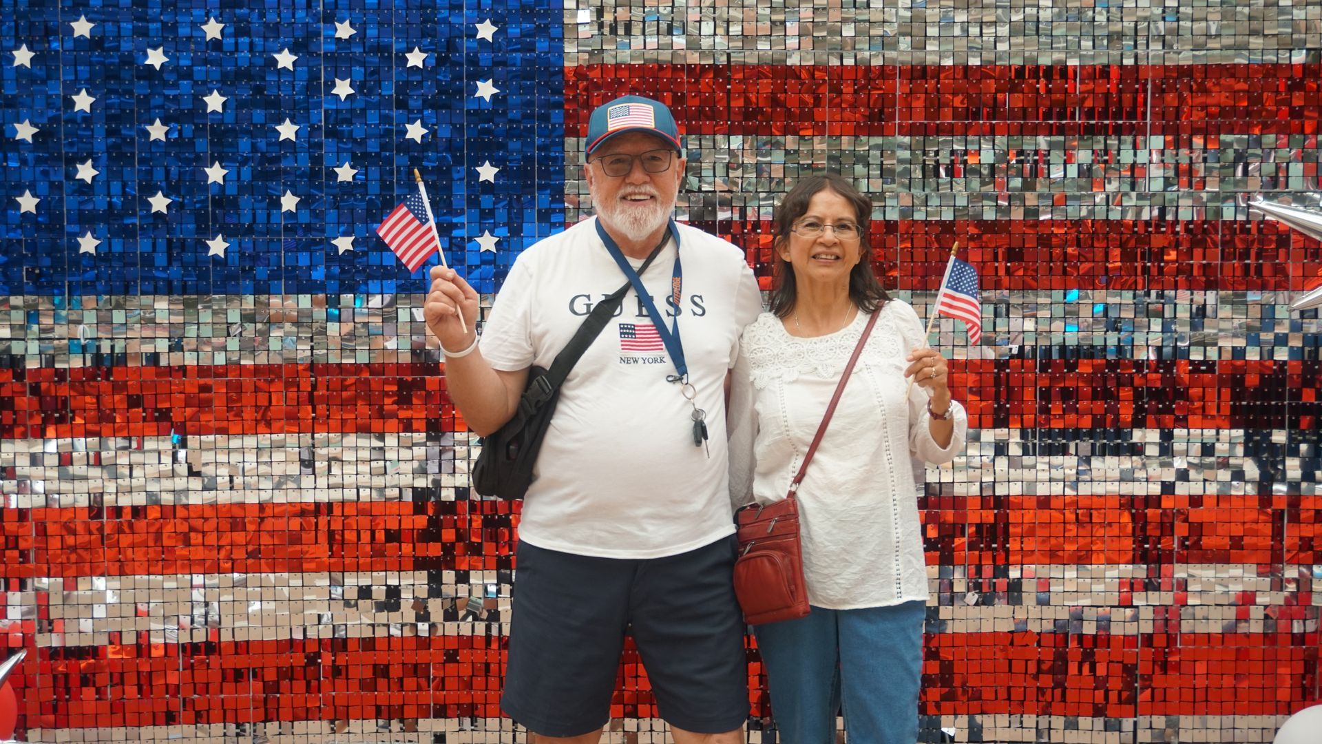Two people posing before a red, white, and blue American flag mural, one holding a small flag.