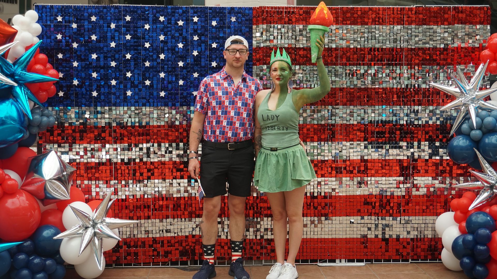 Two people posing in front of a red, white and blue American flag balloon display