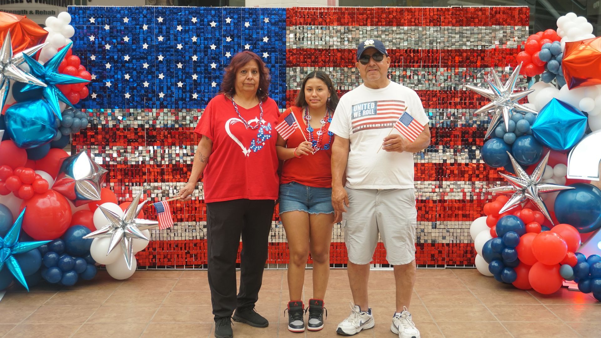 Three people posing in front of a red, white, and blue star-and-stripe balloon backdrop