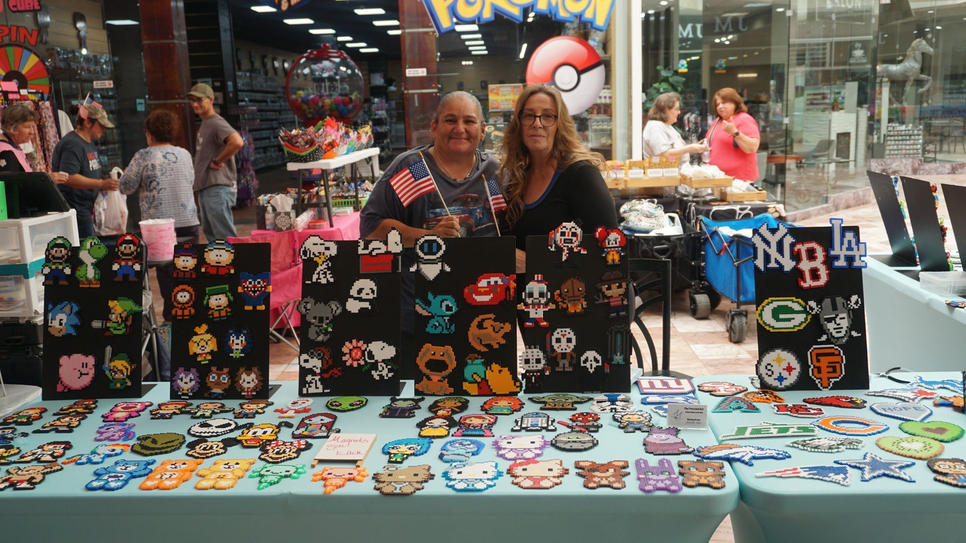 Craft fair table with colorful handmade bags, keychains, and stickers displayed in a mall.