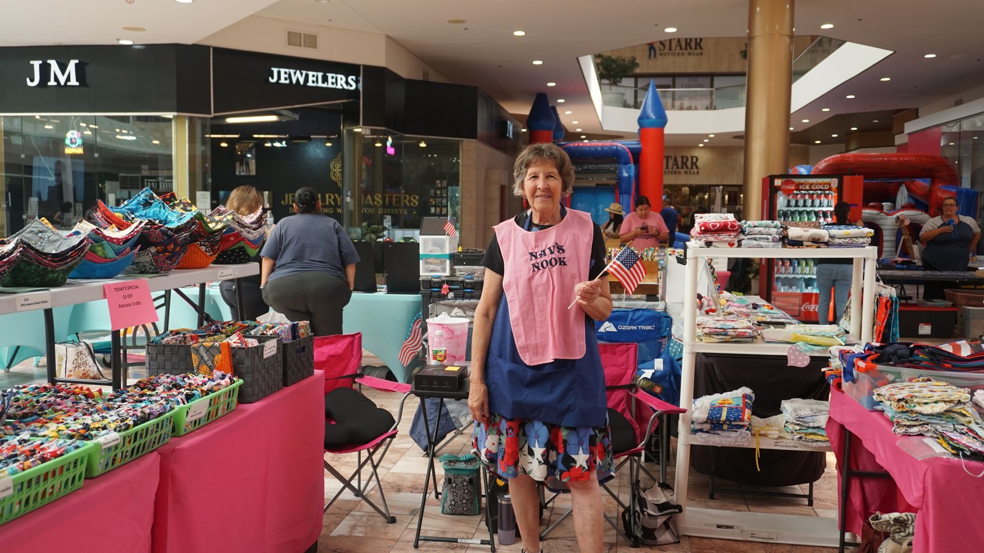 Child standing between colorful toy and craft booths in a mall, surrounded by displays and shoppers
