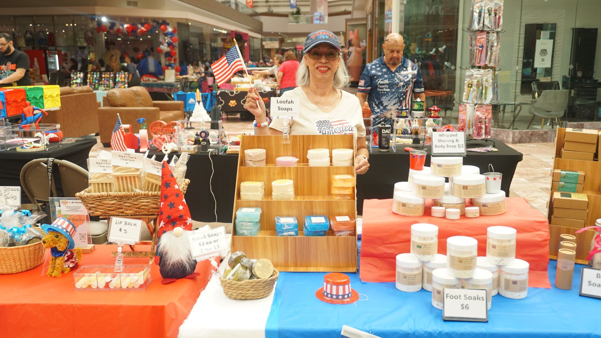 Market stall with jars and packaged goods displayed on colorful tables, vendor standing behind the counter