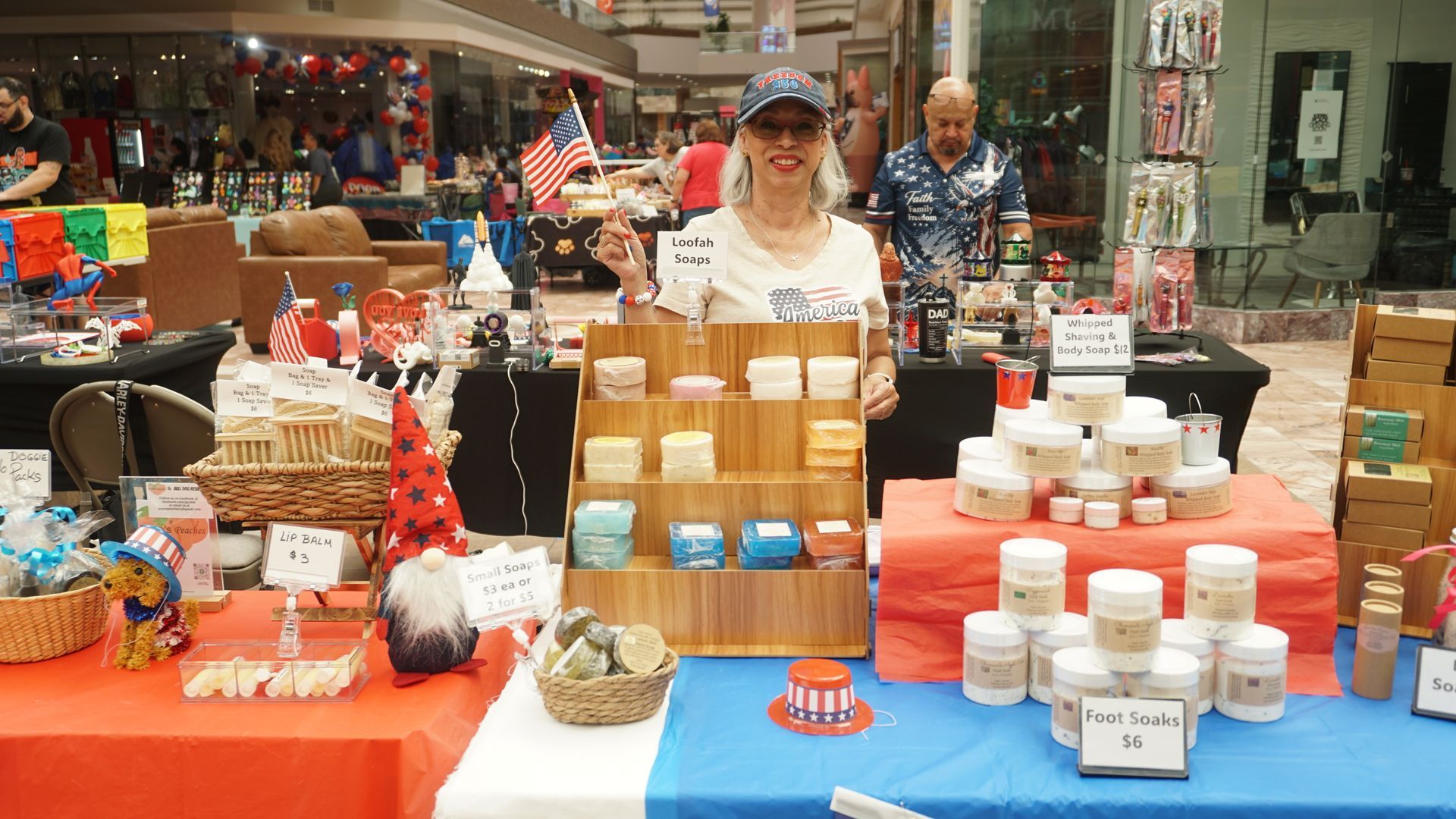 Woman behind market stall with jars and boxes of goods on red and blue tables outdoors