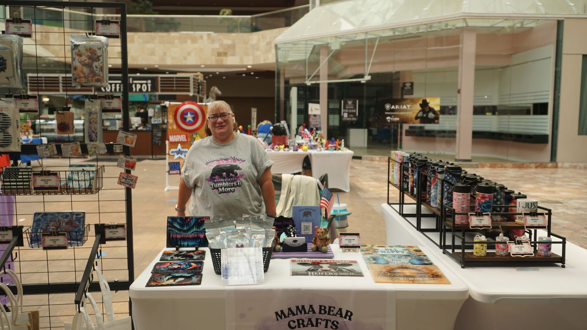 Vendor booth in a mall with a man behind a table displaying merchandise and bins of items.