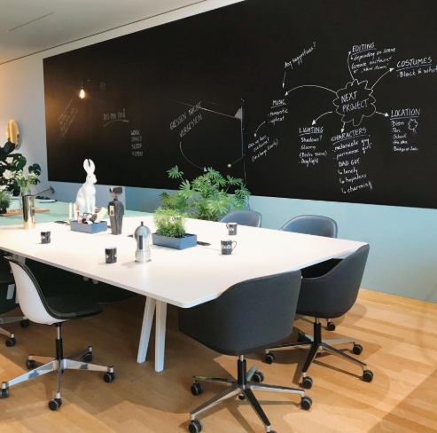 Modern meeting room with blackboard wall, white table, black chairs, and potted plants