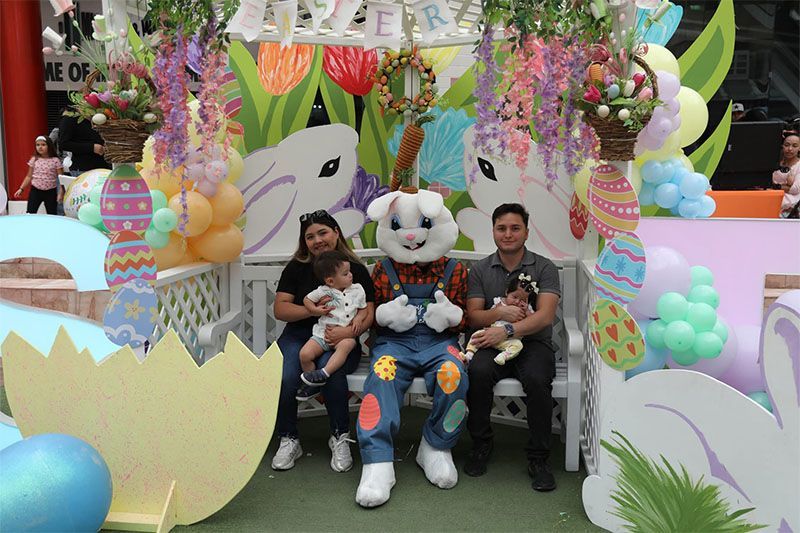 Family seated with a bunny mascot in a colorful Easter-themed display, surrounded by pastel decorations