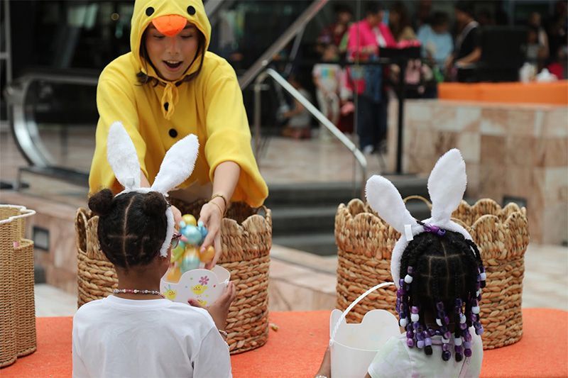 Person in yellow costume hands candy to children wearing bunny ears at an outdoor event.