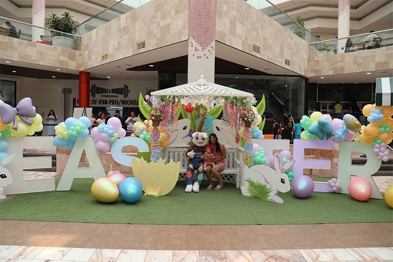 Outdoor mall Easter display with colorful balloons, giant letters, and children posing under a decorated umbrella
