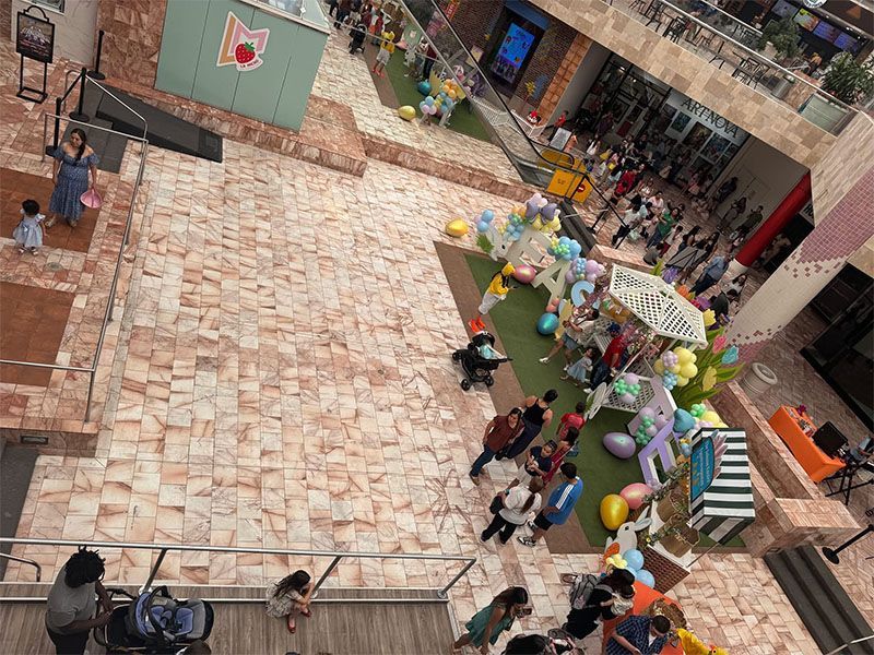 Courtyard with a crowd gathered around a decorated booth, colorful balloons, and striped umbrellas on a brick plaza