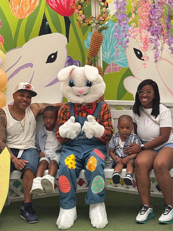Family seated with a white bunny mascot in front of a colorful floral mural