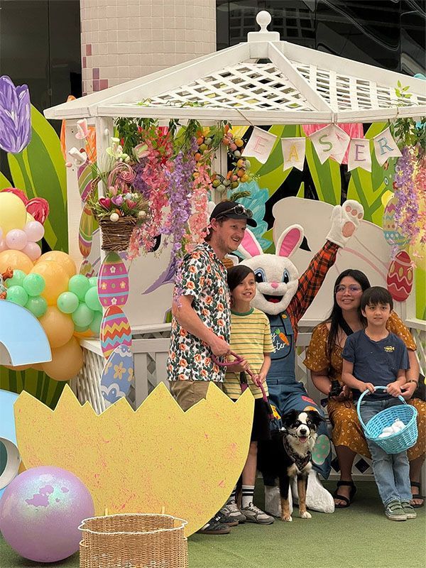Family posing with a panda mascot in a colorful Easter display with a white gazebo and balloons