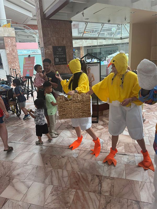 Three people in yellow duck costumes performing indoors near a crowd.