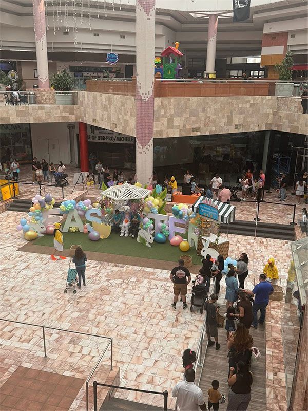 Indoor mall atrium with people gathered around a colorful Easter-themed display and bunny decorations