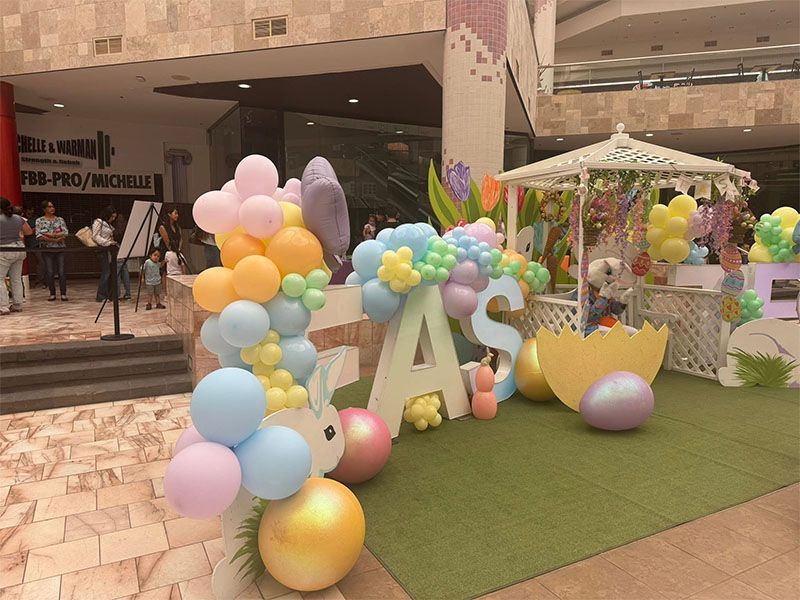 Pastel balloon display with large “1” and “A” letters on a green mat in a mall entrance