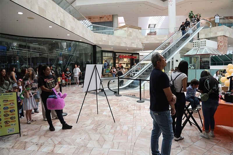 Crowd gathered in a mall atrium near an escalator and performance setup on a tiled floor
