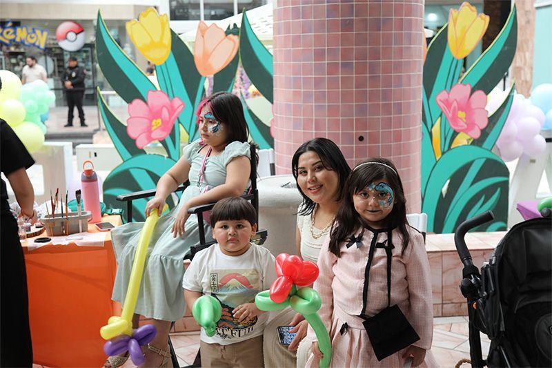 Family at a colorful outdoor event with floral decor, including two children seated in front of an adult woman.
