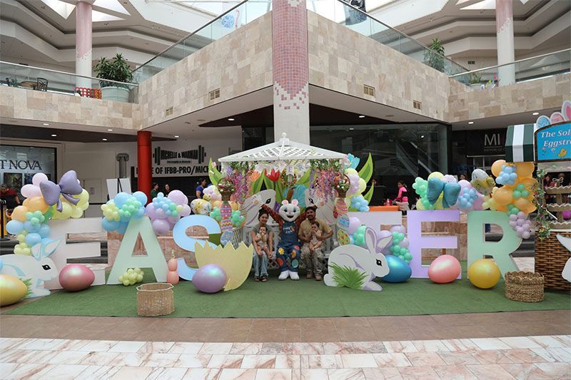 MALL atrium with pastel Easter display, giant letters, eggs, and a flower-covered centerpiece surrounded by decorations