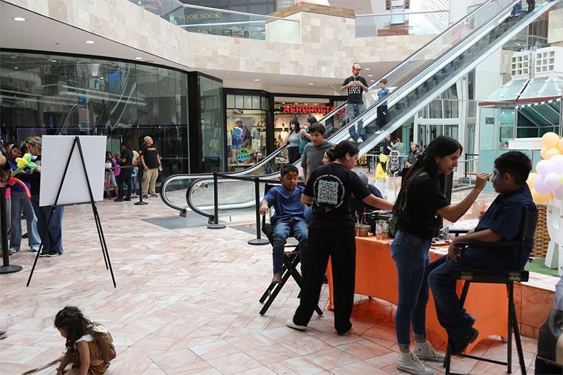 People sitting and chatting in a shopping mall atrium beside an escalator and orange kiosk table