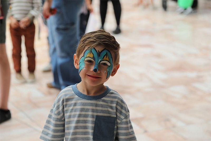 Child with butterfly face paint smiling indoors, wearing a striped shirt.