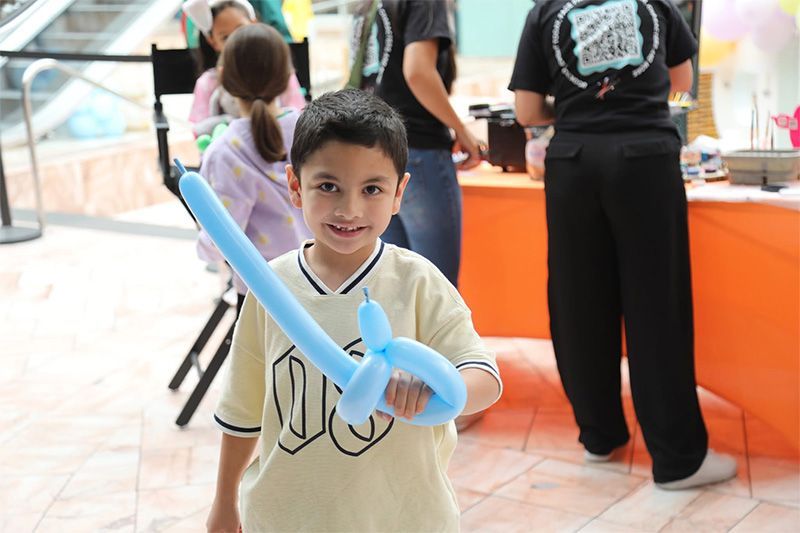 Child holding a blue balloon sword and smiling indoors at a party