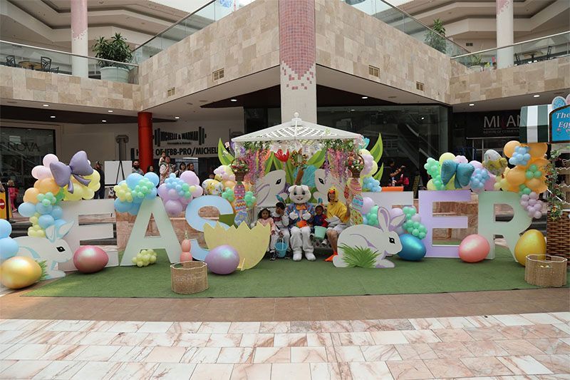 Festive Easter display with large pastel letters, balloons, flowers, and bunny decorations in a mall atrium