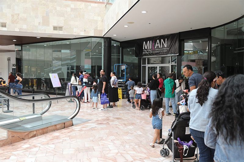People waiting in line outside a store entrance at a mall, with shopping bags and a fountain nearby