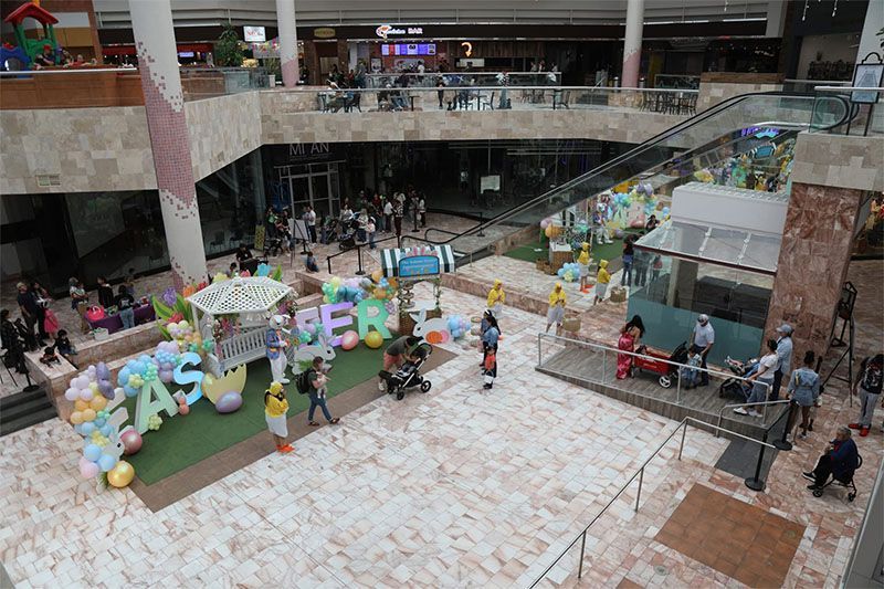 Indoor mall atrium with colorful balloon display, people walking, and seating areas around a central event space