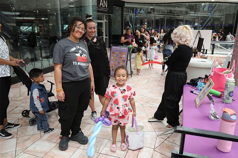 People at a mall event with balloon animals, including a child in front and colorful costumes nearby